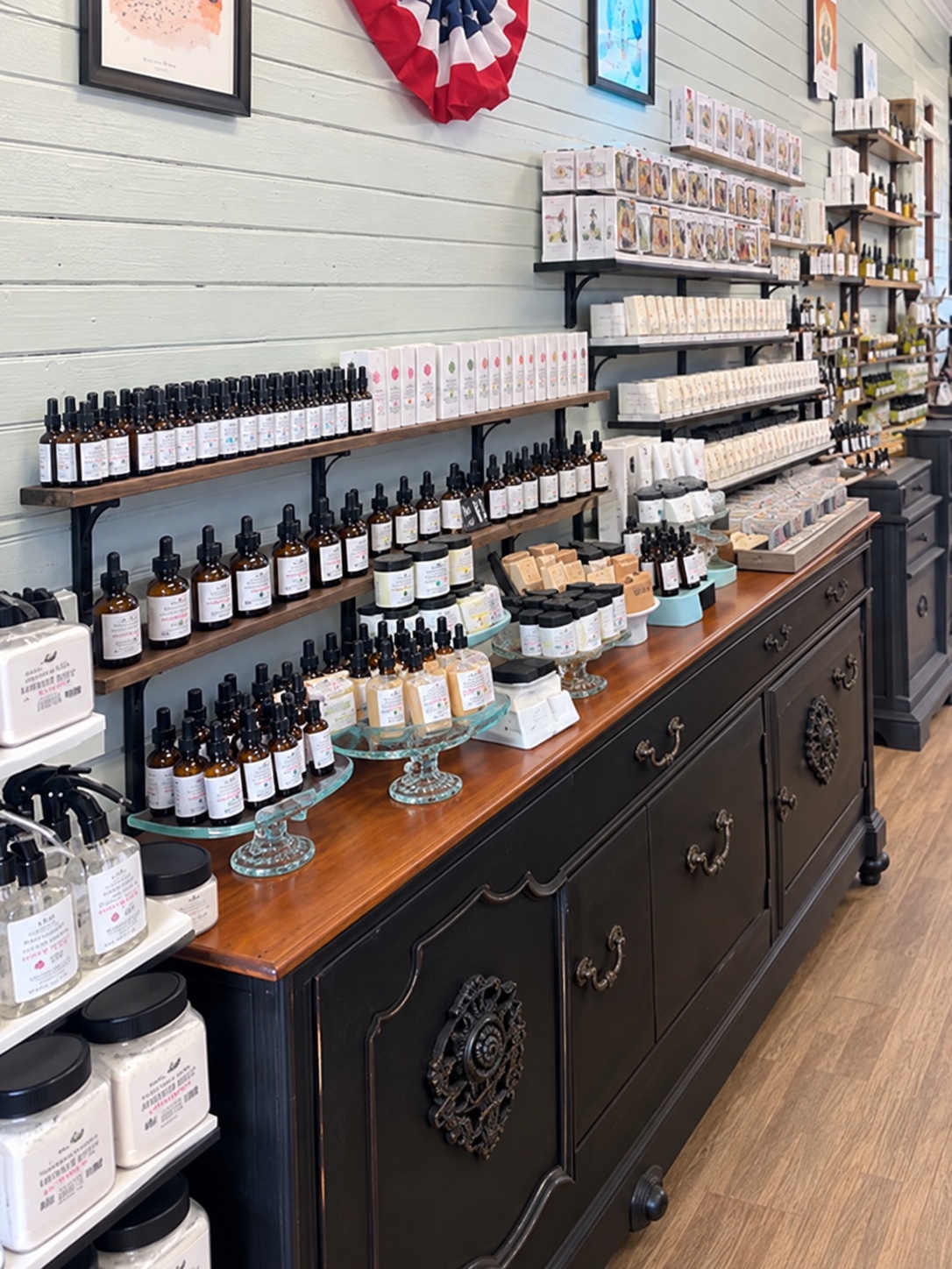 Wall of dropper bottles, jars and boxed soap on shelves above a black antique cabinet